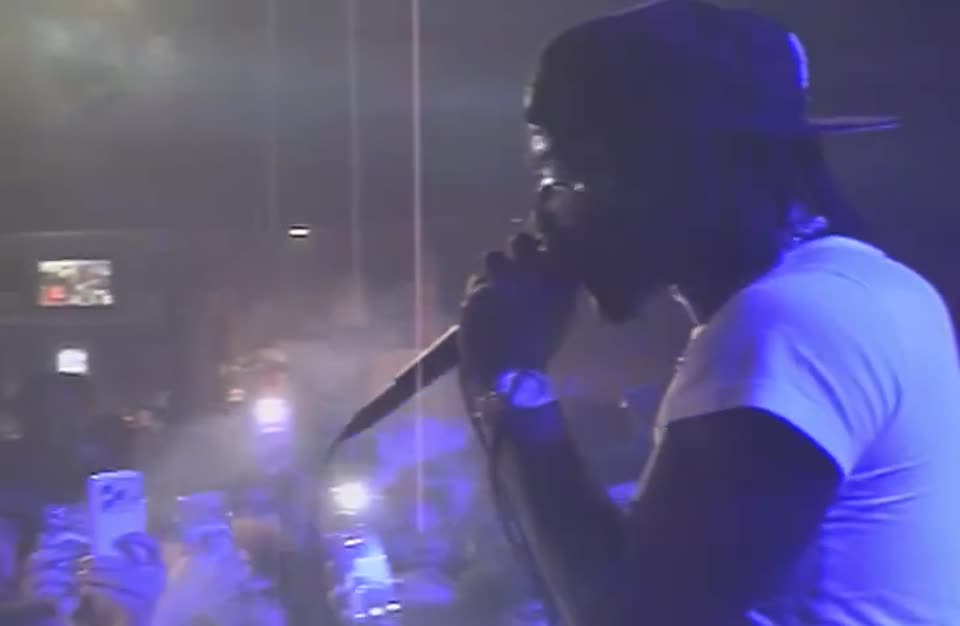 Performer in a white tee rapping into the mic, crowd phones below